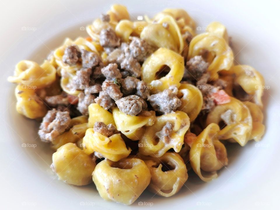 Italian pasta with minced beef and cheese sauce on a white plate.