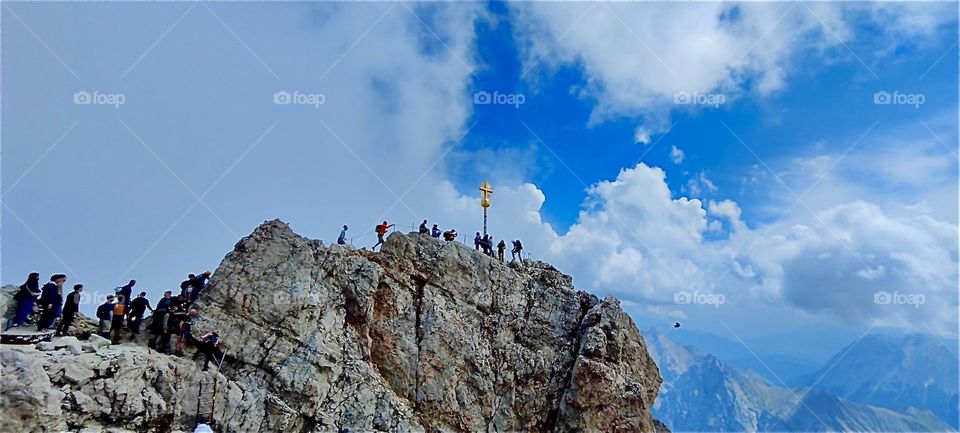 A group of dedicated mountaineers under blue skies lines the ridge mountain that leads to the summit of the “Zugspitze”. At 2962 m it is the tallest mountain in the German “Alps”. 2024. Hypnotic Productions