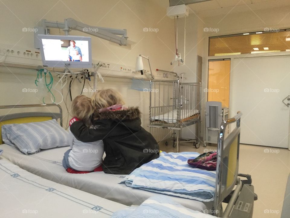 big sister holding her sick little sister in a hospital.