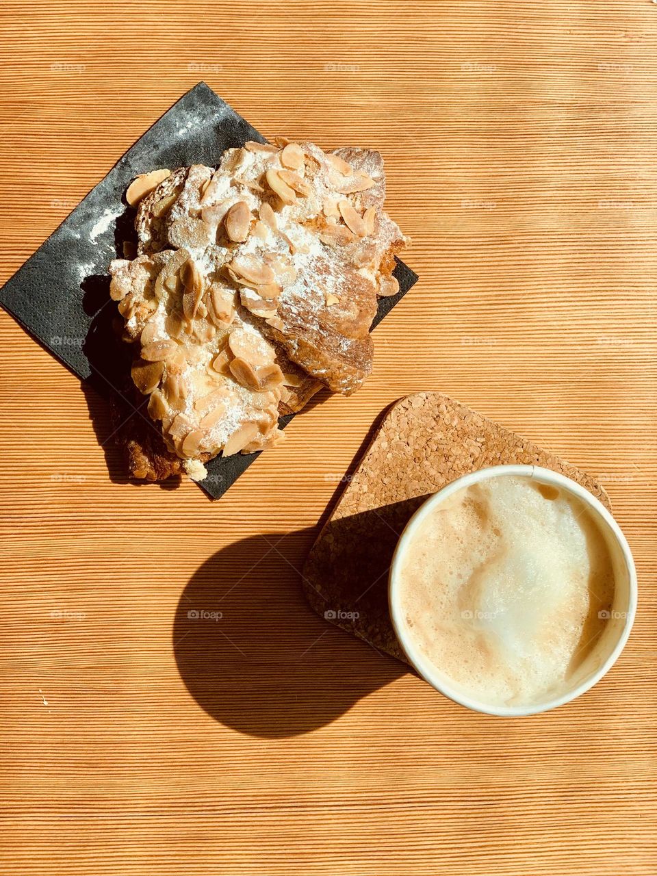 Hot beverage mug and almond croissant seen from above on wooden surface 