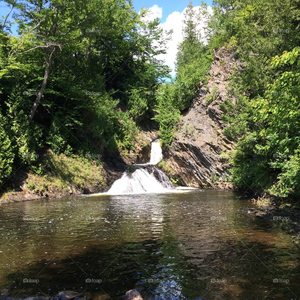A rocky waterfall with lush greenery and a beautiful pond. 