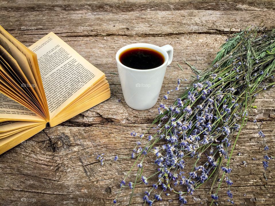 Open book with lavender and cup of coffee beside placed on wooden table