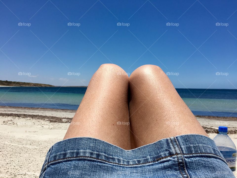 Point of view woman facing ocean laying on beach, bare knees showing and wearing denim skirt 