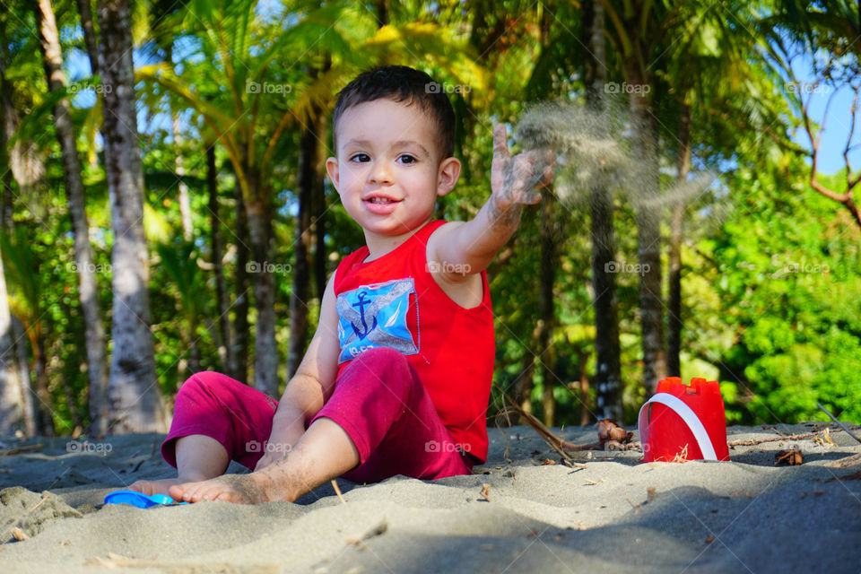 Little boy playing with the sand on the beach, enjoying the summer