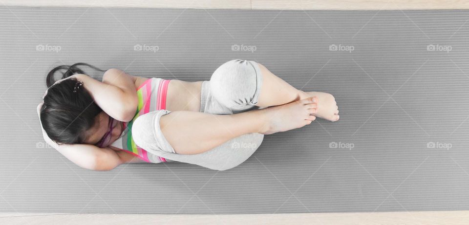 One little caucasian girl doing an exercise lying on a gray rug on a wooden floor in a room on a summer day, flat lay close-up.