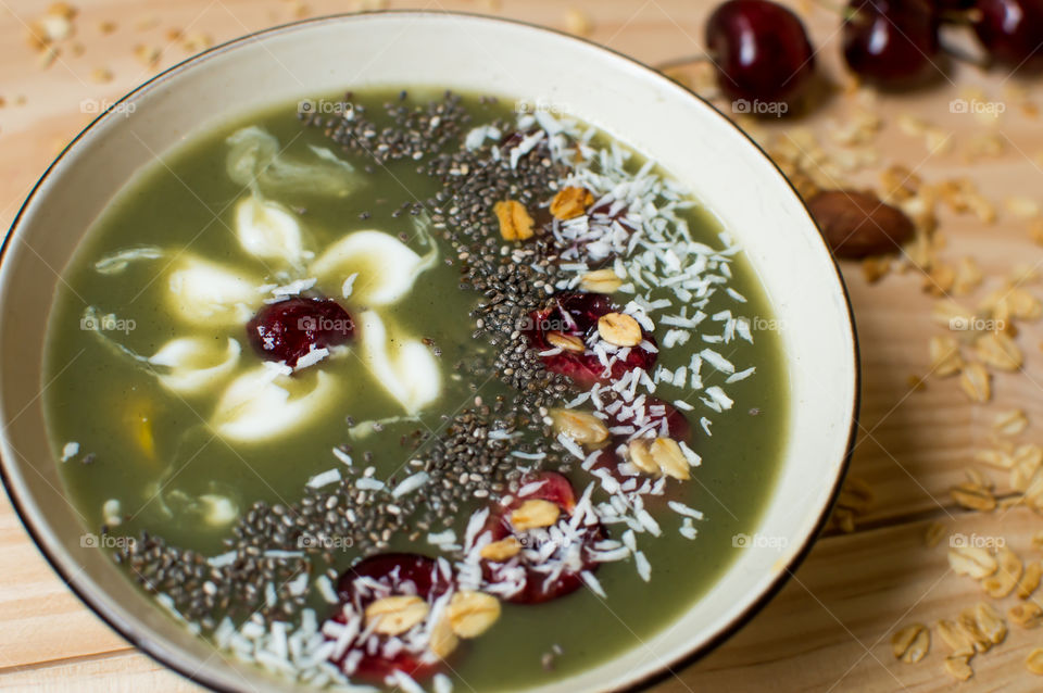 Beautiful green artisanal smoothie with delicate flower fruit garnish with yogurt, crunchy honey granola, coconut, dark cherry, chia and almonds close-up full frame food photography 