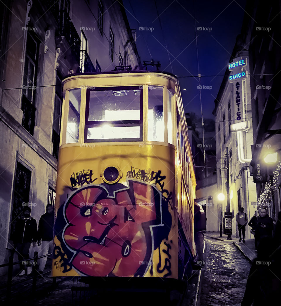 A graffitied tram car ascends up hill in this nighttime shot in Lisbon