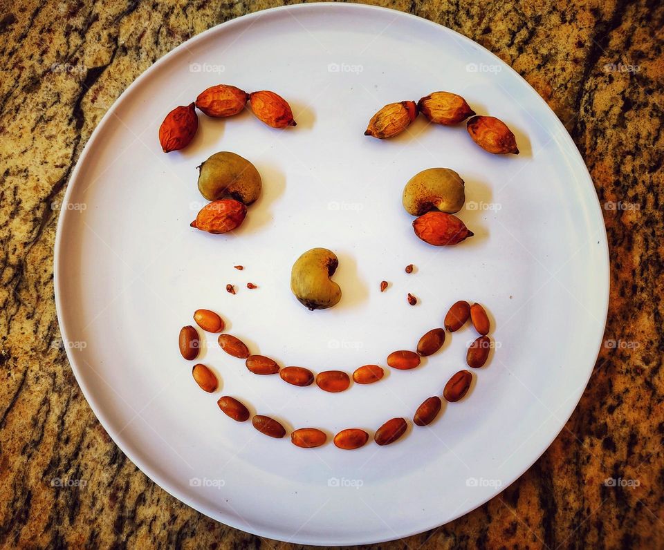 a white circular plate, in the shape of an emoji smiling all happy, made with several types of seeds.