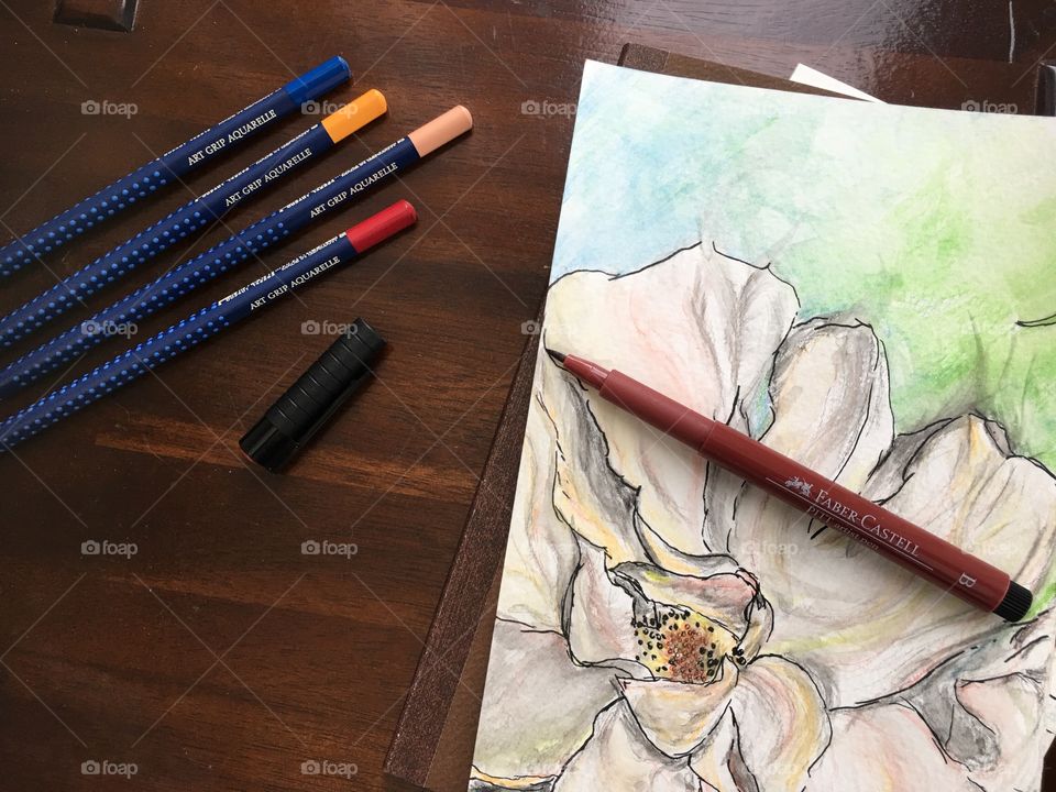 Flat lay Watercolor sketch of flower on Wood table and sketchbook with colorful Faber-Castell PITT Artist pens and Art Grip Pencils 