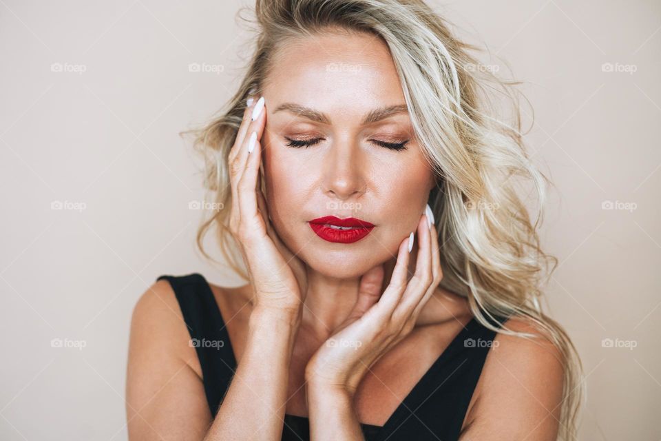 Close up portrait of beautiful blonde young woman with bright makeup and closed eyes in evening dress on beige background