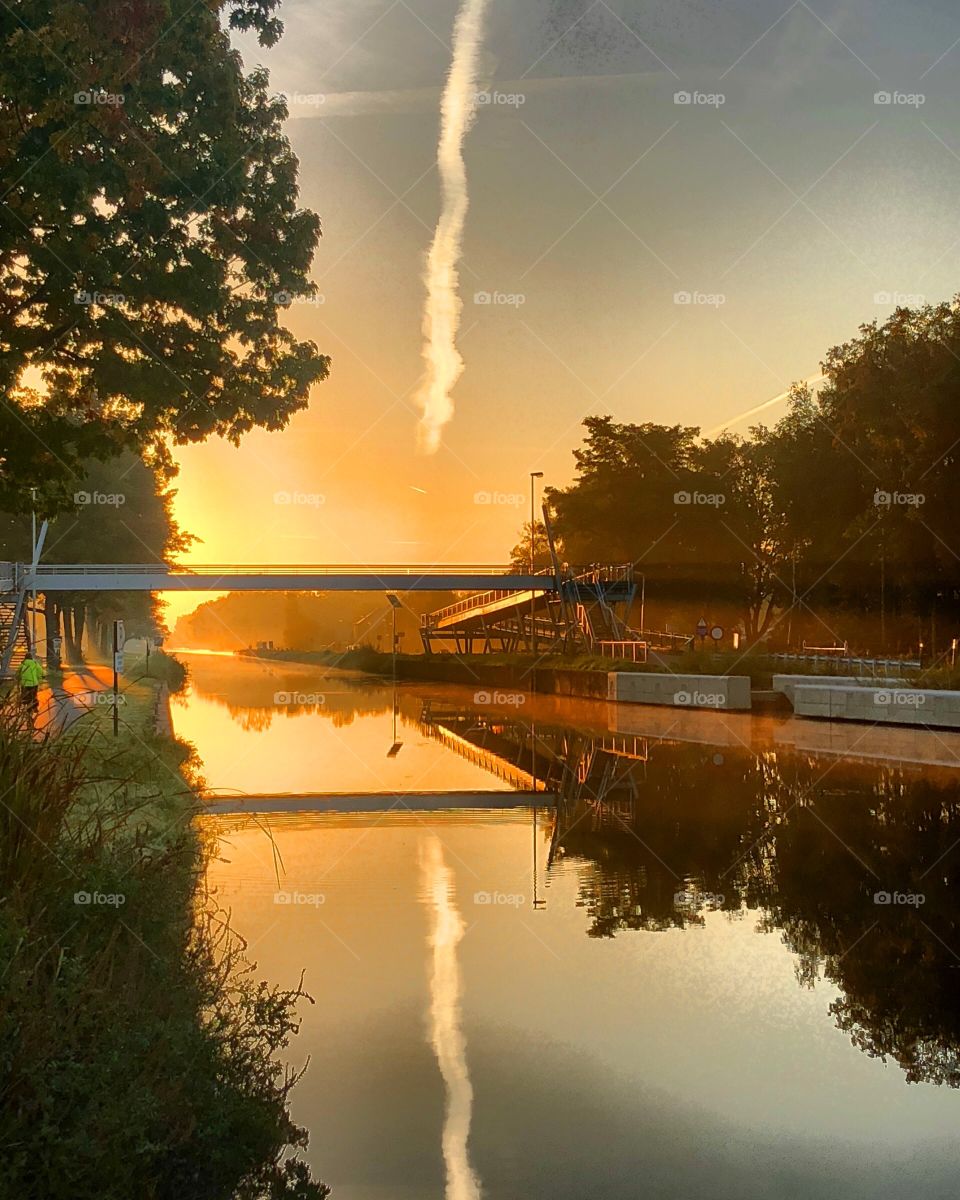 Golden sunrise reflected in the water of the river flowing through a rural landscape