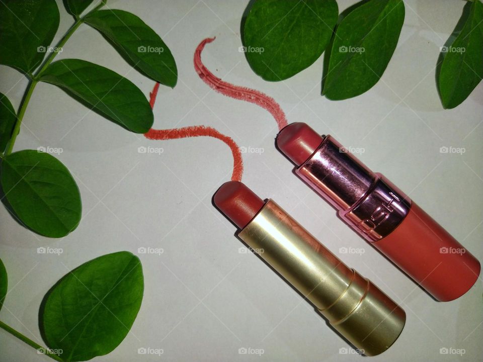 Lipsticks in the middle of green leaves against a white background.