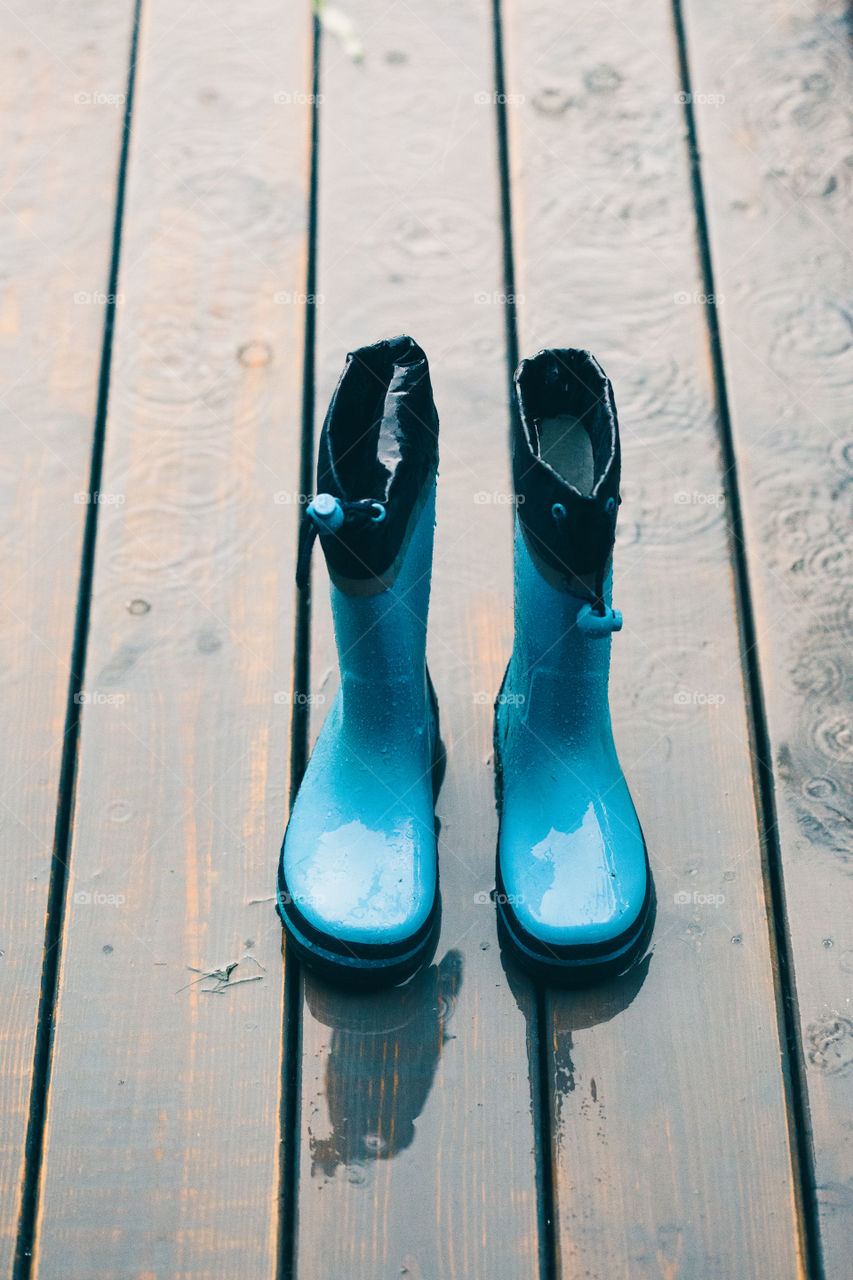 Row of wellies in various sizes standing on a wooden porch while raining