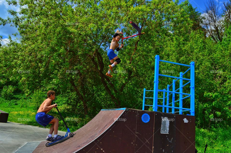 several young people perform tricks on stunt scooters flying up in the air over the ramp