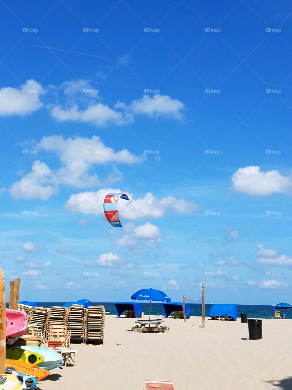 Parasailing high in the sky over a beach. The sky is blue with an umbrella set up early in the beaching day.