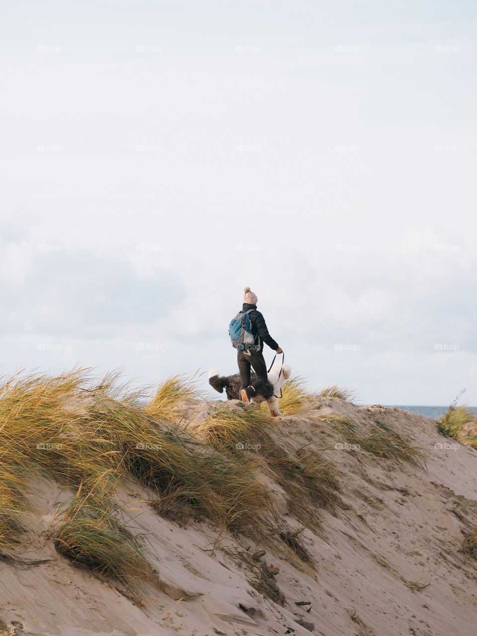 Young woman walking with big fluffy dog on seaside in sunny autumn day