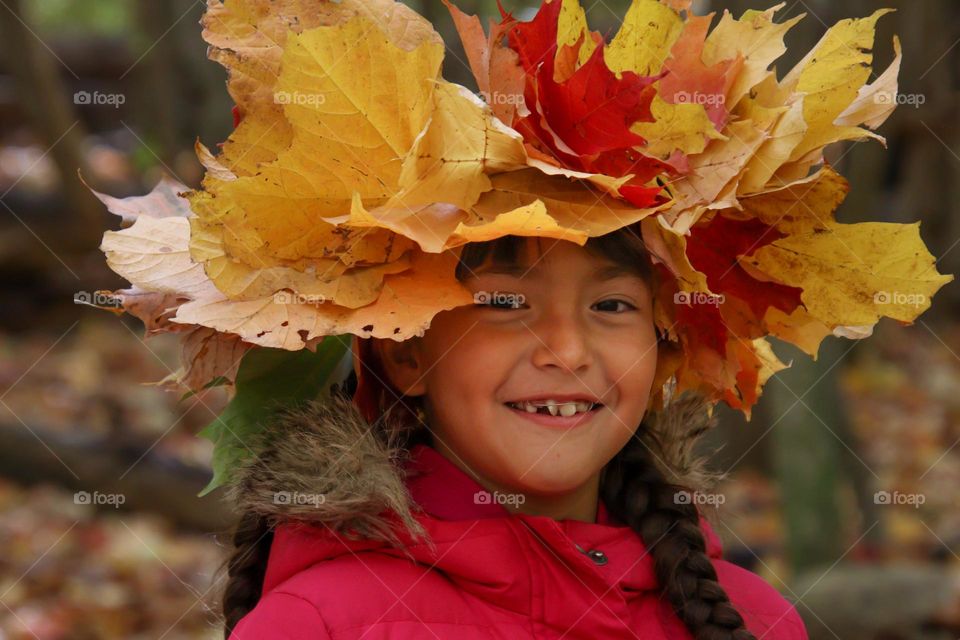 Happy cute little girl in a crown of autumn leaves