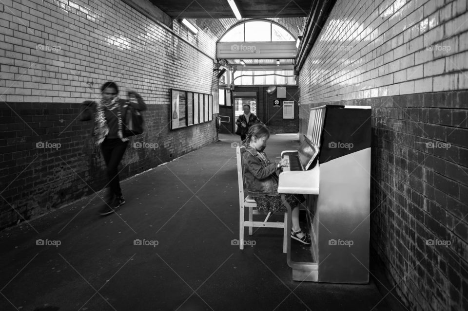 Little girl playing piano in subway passage.