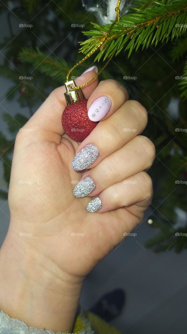 A female hand on the background of a New Year's, green Christmas tree with garlands and balls.
