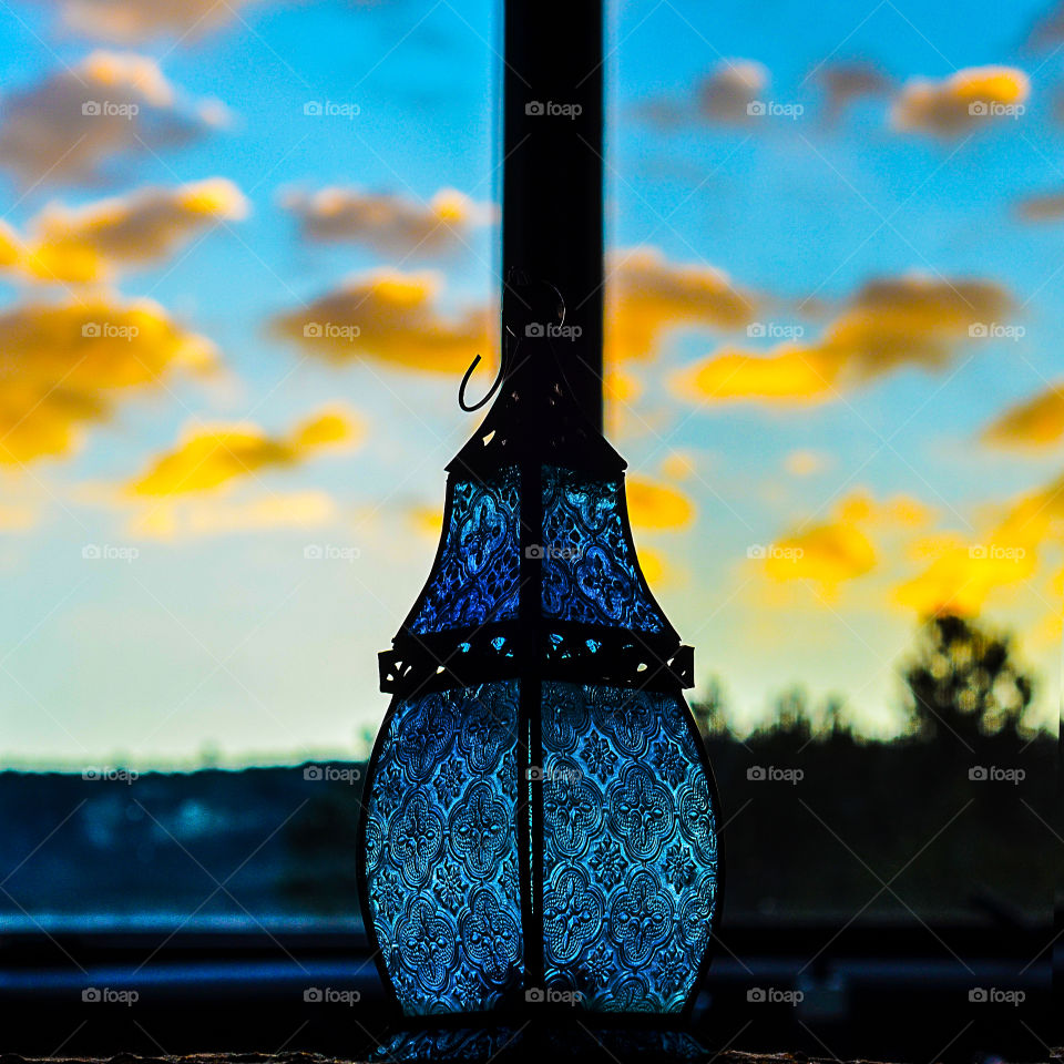 elegant elaborate small blue Glass lantern glows against the yellows and blues of a southwestern sunset sky