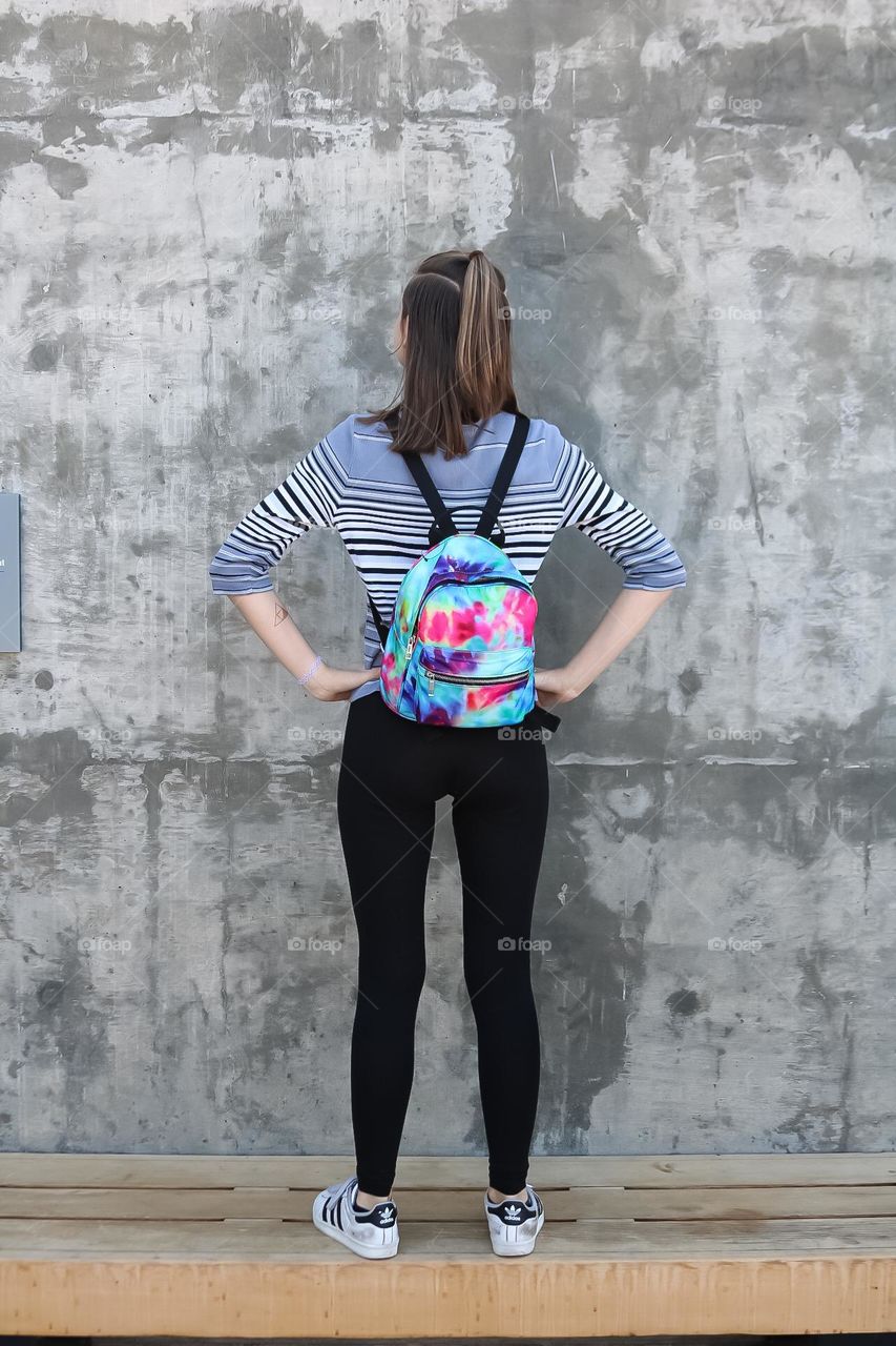 Striking a pose in front of a cement wall with a tie dye style backpack ready to explore the world 