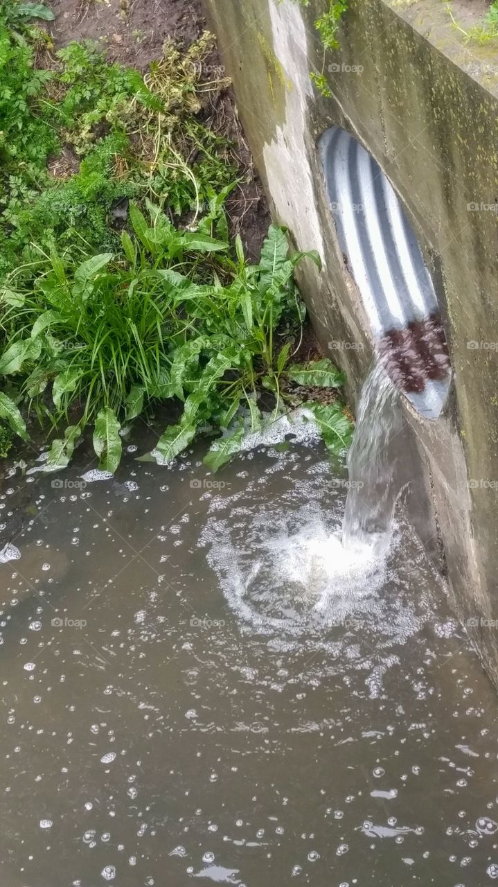 rain water flowing through culvert into drainage ditch
