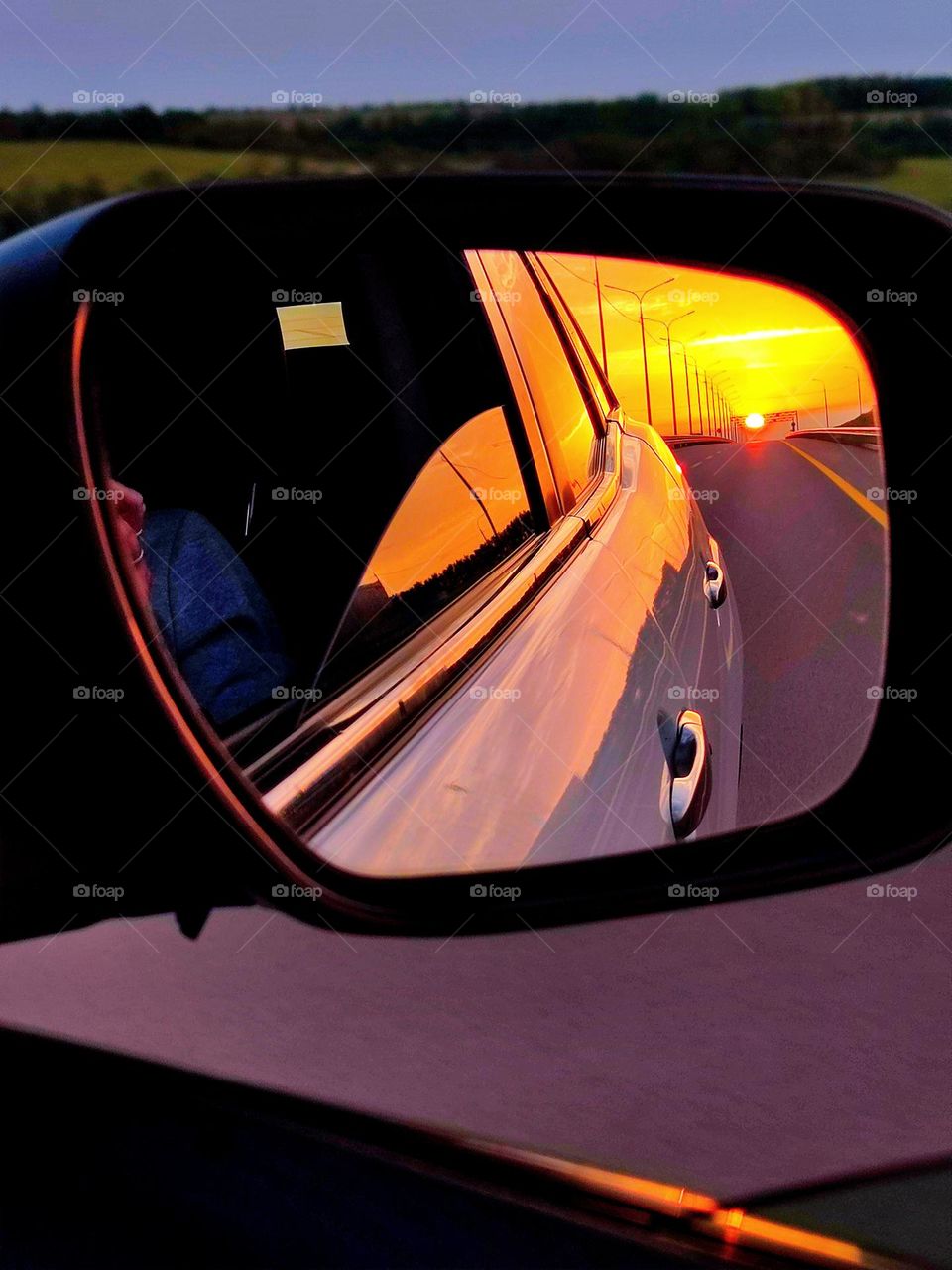 View from the car. Reflection in the side mirror of a sunset. You can see the road of the autobahn, on the horizon of which the red sun sets