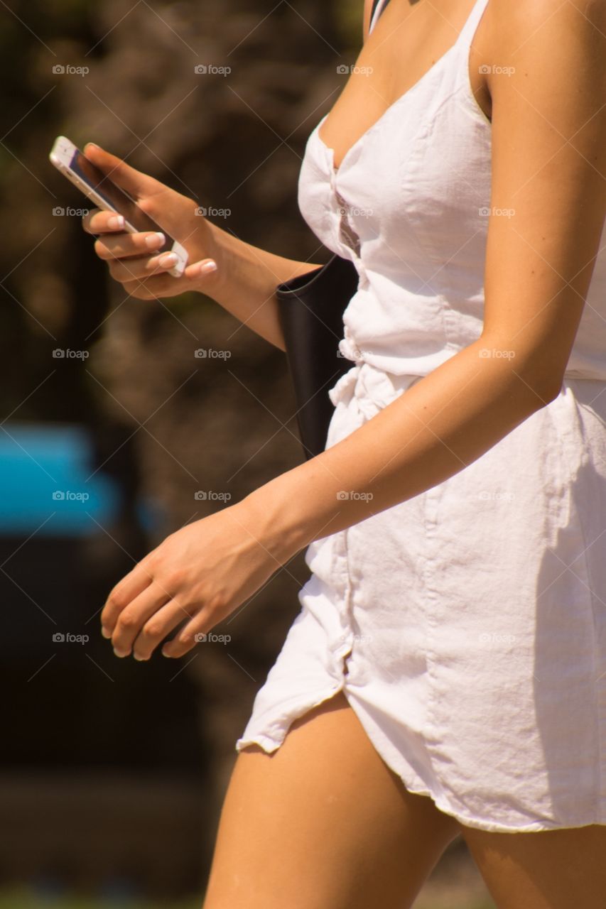 A woman walking around in her white dress and a phone in her hand