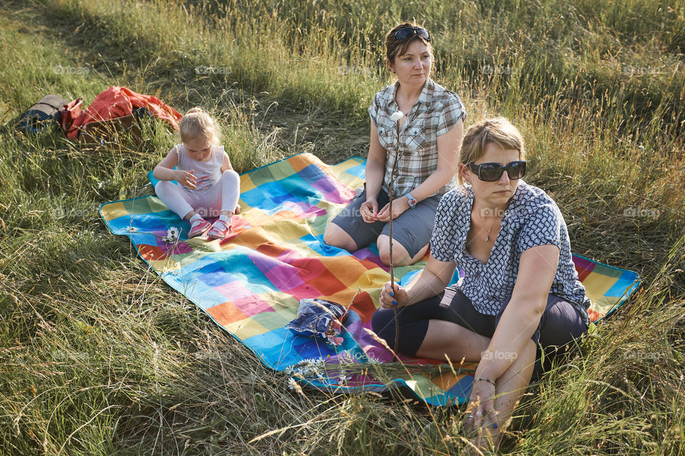 Family spending time together on a meadow, close to nature, roasting marshmallows over a campfire, parents and children playing together and sitting on a blanket on grass. Candid people, real moments, authentic situations