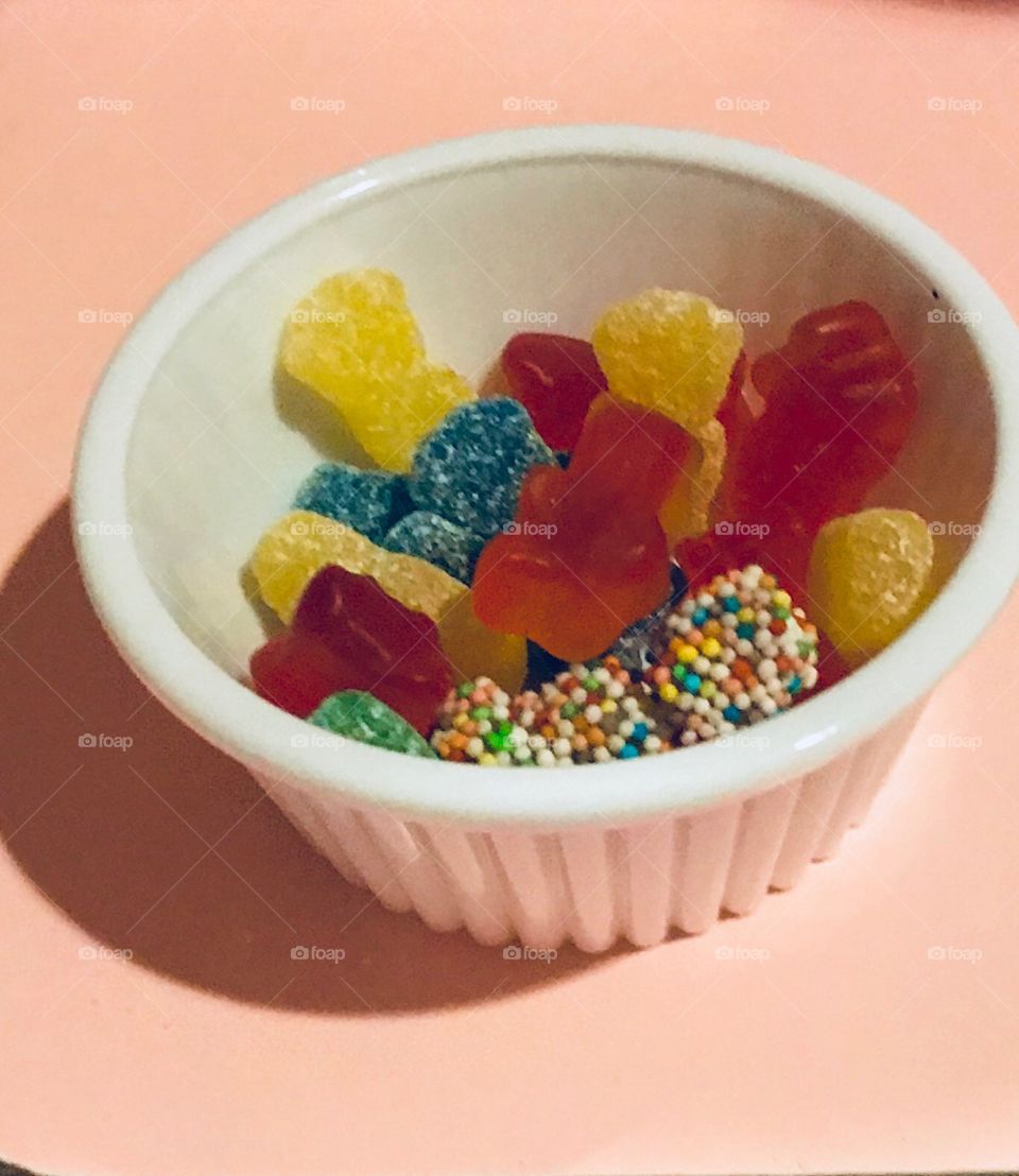 Variety of vibrant and tasty Kids candy in a small white bowl sitting on a pink background 