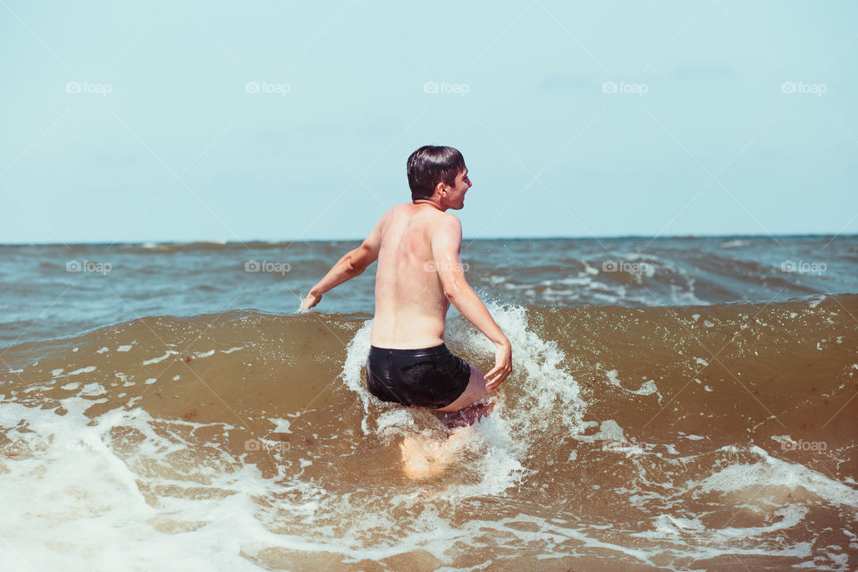 Young man enjoying the high waves in the sea during a summer vacations. Spending a summer holiday by the sea