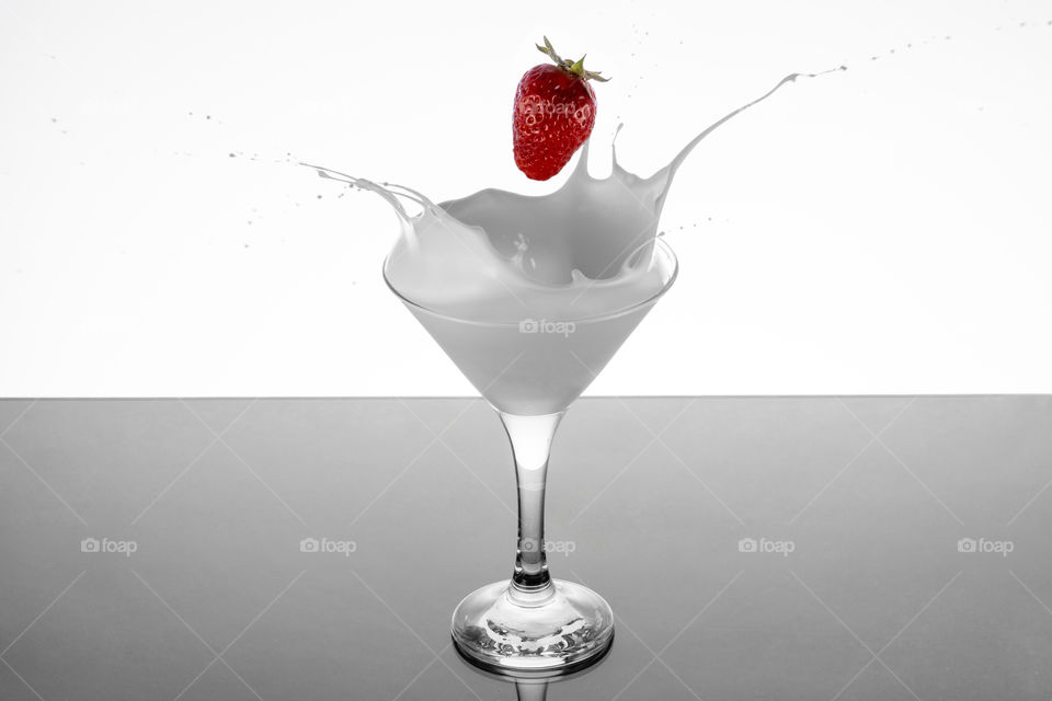 Fresh strawberry falling into glass of milk
