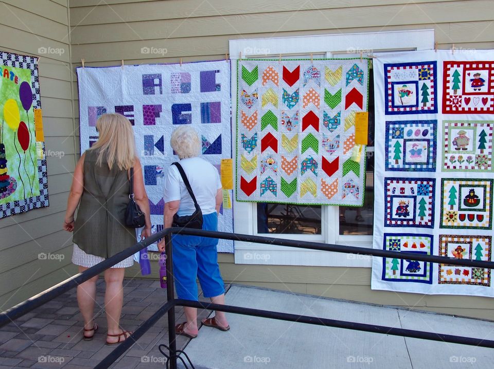 Two woman view with appreciation a row of beautiful quilts at the Annual Sisters Quilt Show in Central Oregon on a sunny summer day in July. 