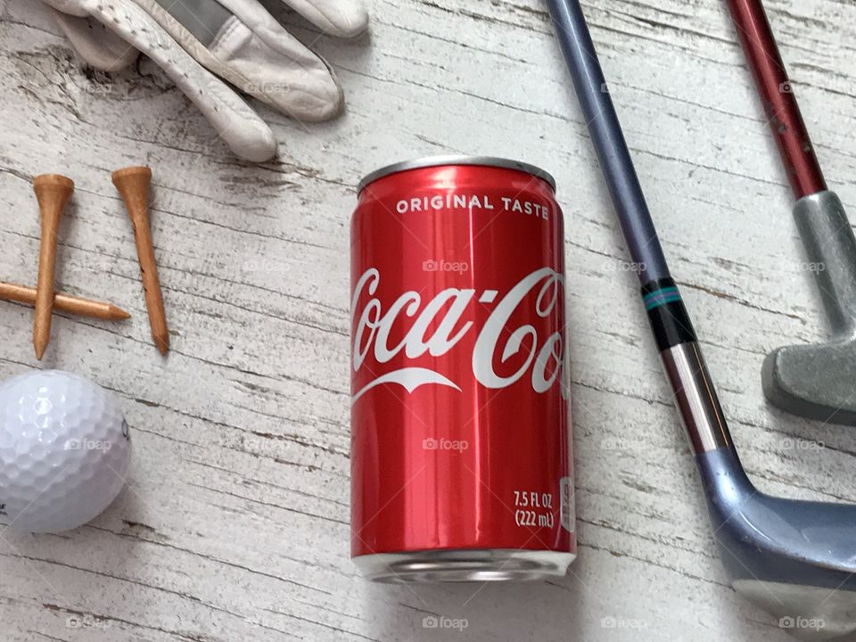 A can of Coca Cola and golf equipment on a rustic white background 