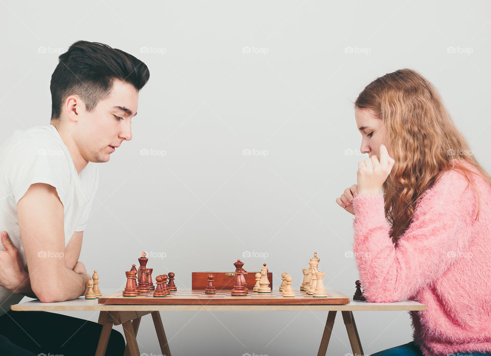 Girl and boy playing chess at home, they are concentrated on their next moves. Teenagers sitting by a table. Profile view. Copy space for text in the middle of image