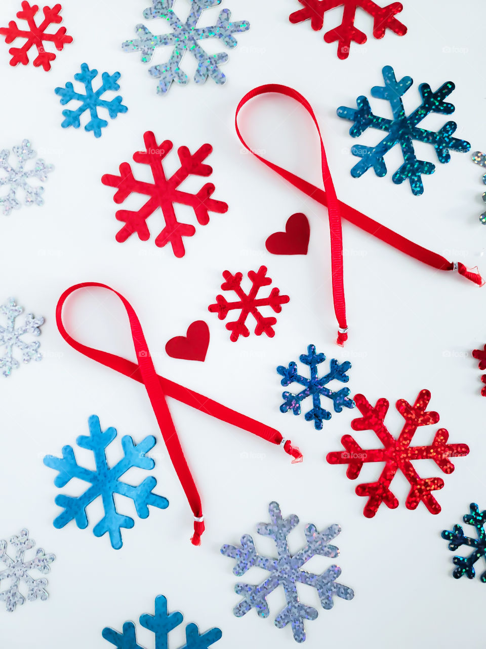 Winter heart disease awareness. Research has shown heart attacks are more common and more severe during cold winter months. Flat lay of two symbolic heart disease red ribbons, with two small hearts and sixteen red, silver and blue snowflakes.