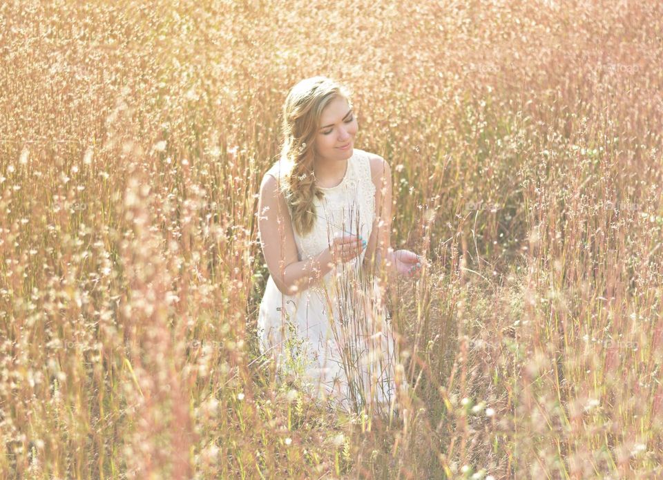 A young woman admired the earth in a golden field in summer in a white dress and flowers in her hair 