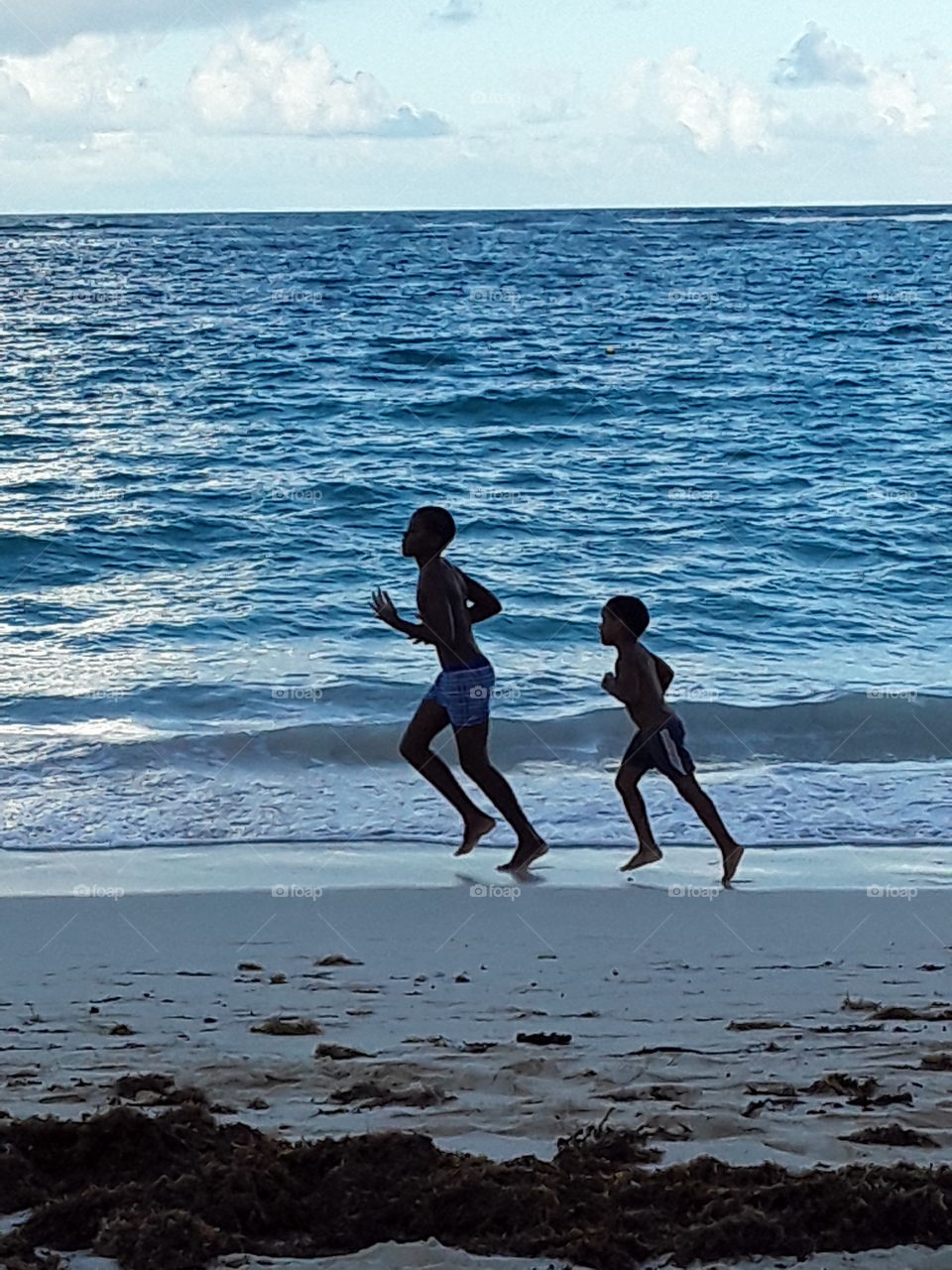 two boys run along the ocean