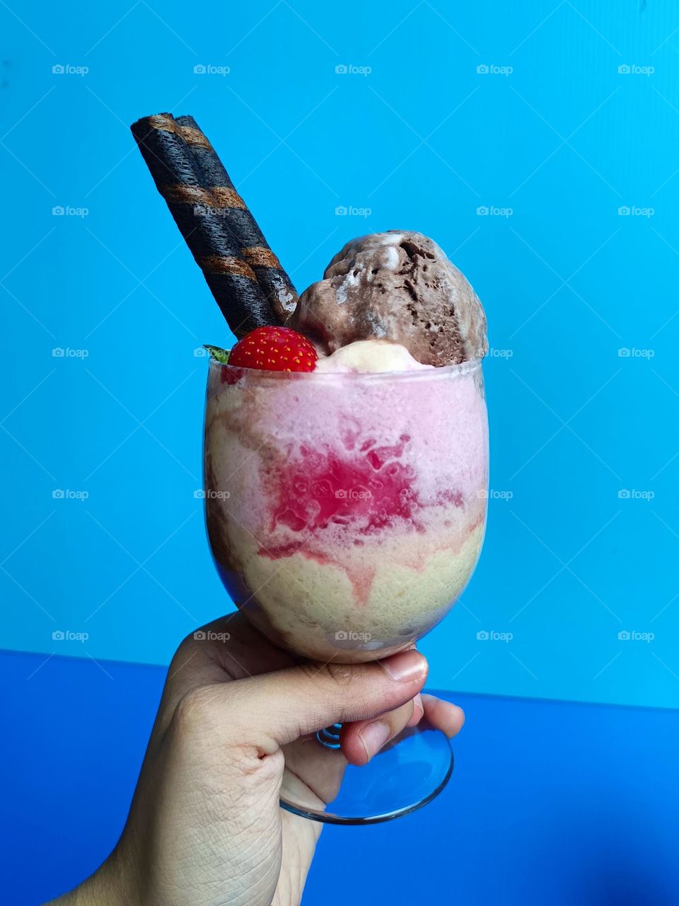 Ice cream in a glass decorated with strawberry and wafer rolls on blue background.