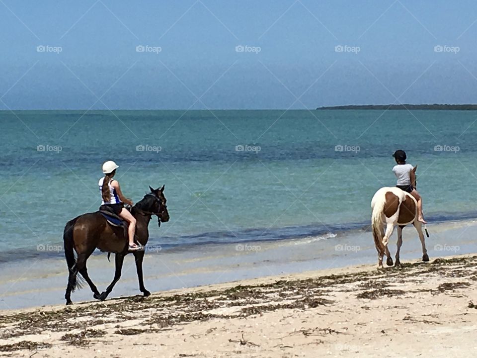 Two girls horseback riding on beach along seashore