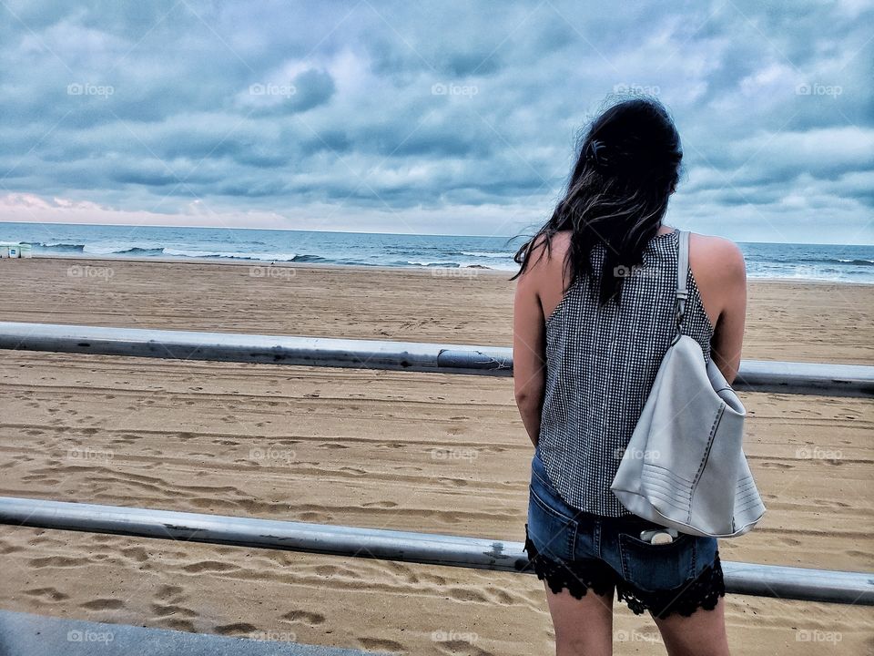 Lone woman looking at ocean from beach boardwalk.