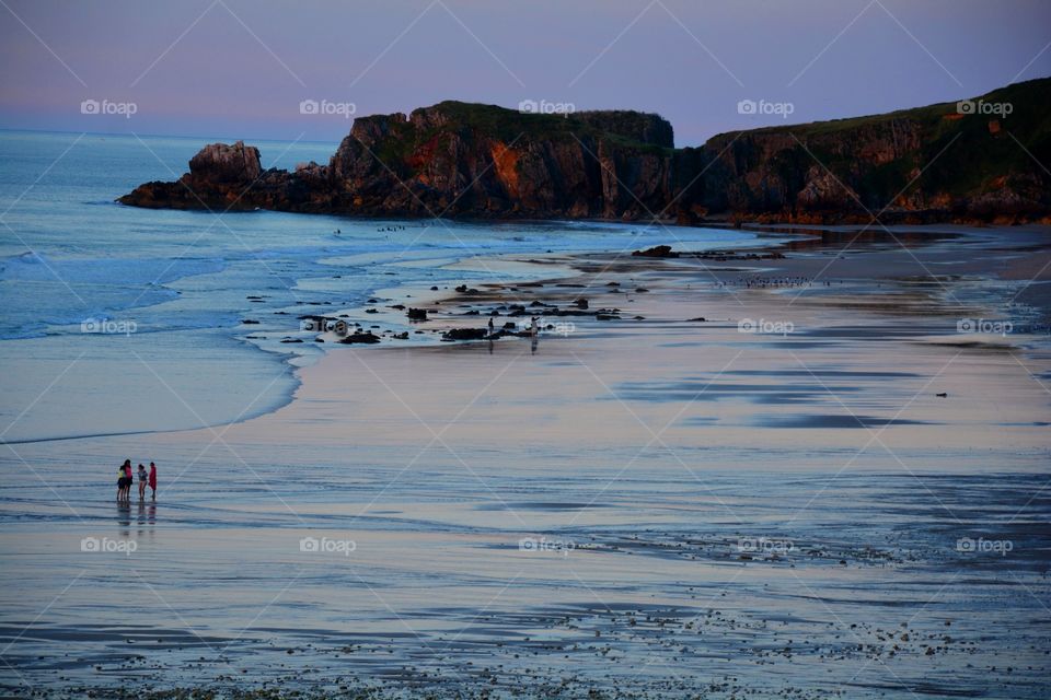 people walking in the seashore during the sunset, rocks andcliffs