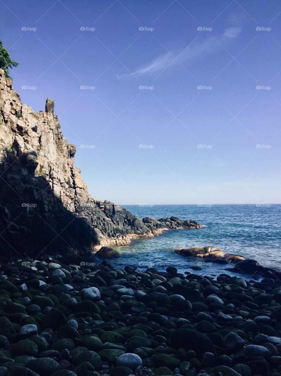 Rocky shore overlooking the blue, Baltic Sea off the island of Bornholm. Cliffs with trees tower over the beach. 
