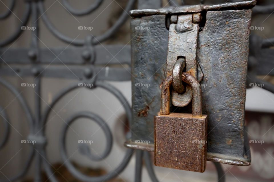 Closeup of an rusty metal padlock hanging tightly closed on an old metal gate 