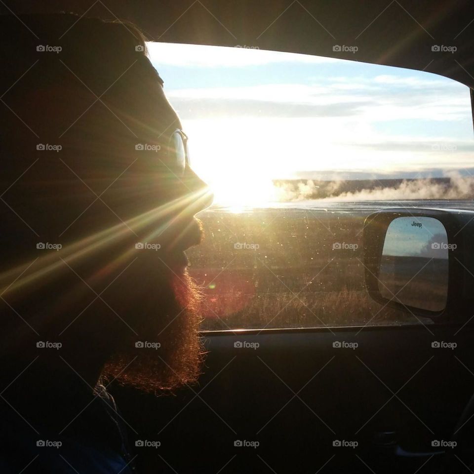 sunset driving on a road trip to Yellowstone national park's hot springs silhouetted bearded man on a road trip in a jeep