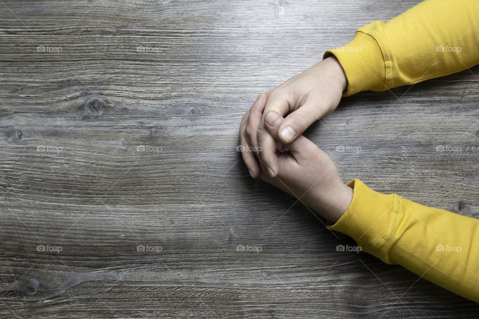 Men's hands in a yellow jacket lie on a gray wooden surface, which is used as a background or a surface with incident light