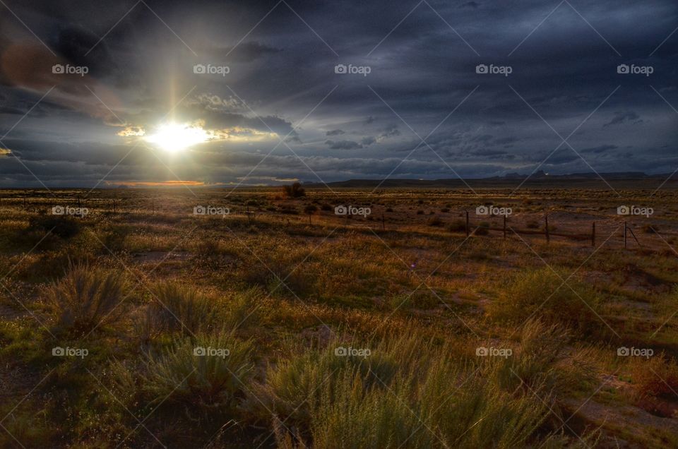 From behind the clouds the sun is sending its last rays across the large and rusty fields from the feet of the Capitol Reef Mountains in Utah. It is a magical moment bathed in an inspiring last illumination. 