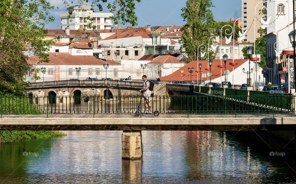 A man on a scooter crosses a bridge over the Rio Nabão on a summer’s day, in the city of Tomar, Portugal 