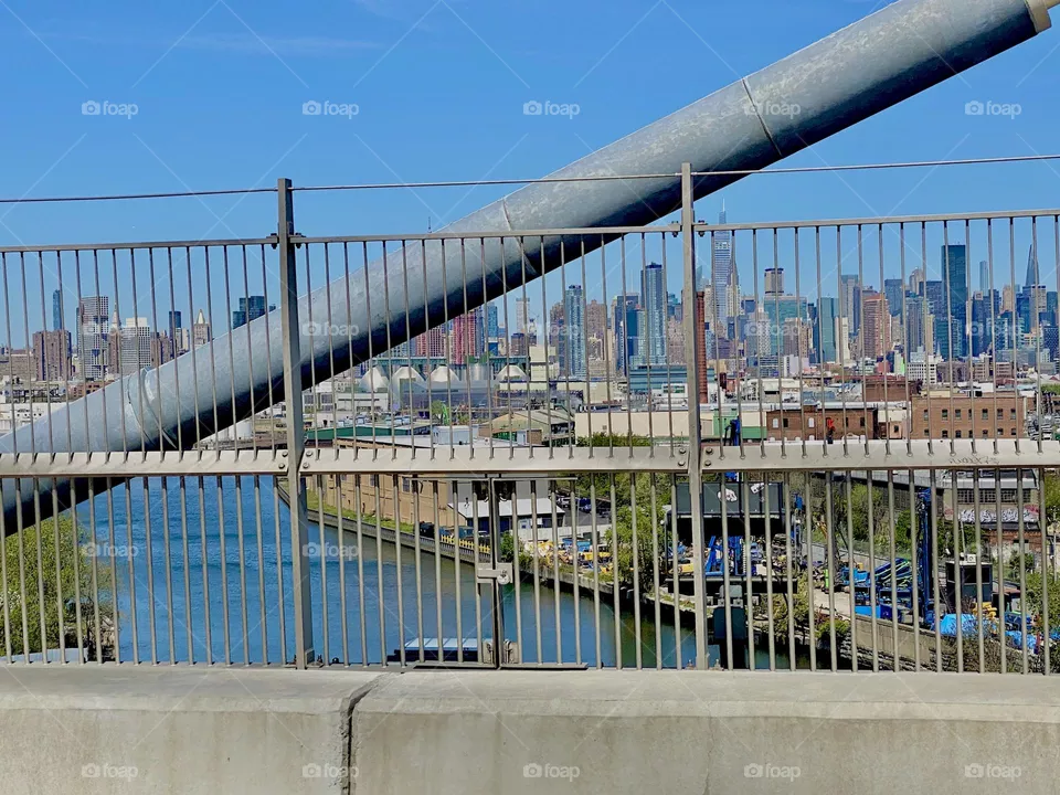 A sideways bar of the „Kosciuszku Bridge“ which is a modern drawstring bridge spanning the E River at „Newtown Creek“ from LIC, Queens into Brooklyn, NY. The East River is visible below and Manhattan in the far distance. 2022. Hypnotic Productions