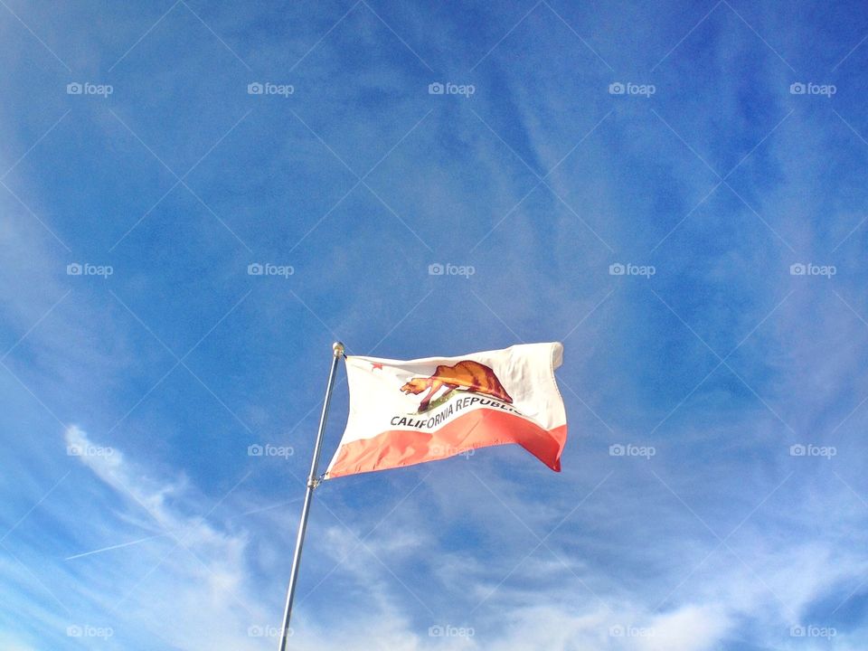 California Republic. The California State flag flies in the wind against a bright blue sky with white clouds.